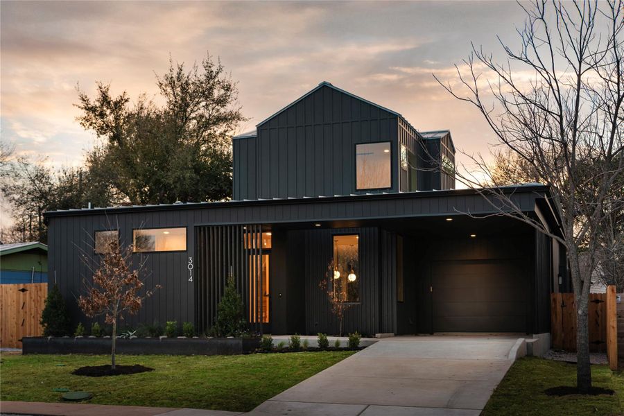 View of front of property with concrete driveway, a lawn, board and batten siding, fence, and a garage