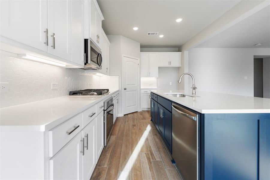 Kitchen with white cabinets, stainless steel appliances, recessed lighting, blue cabinetry, and a center island with sink