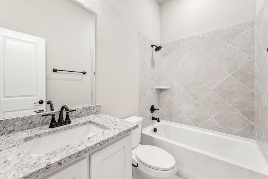 Full bathroom with granite vanity, white cabinets, and tub-shower combo with diagonal tile surround