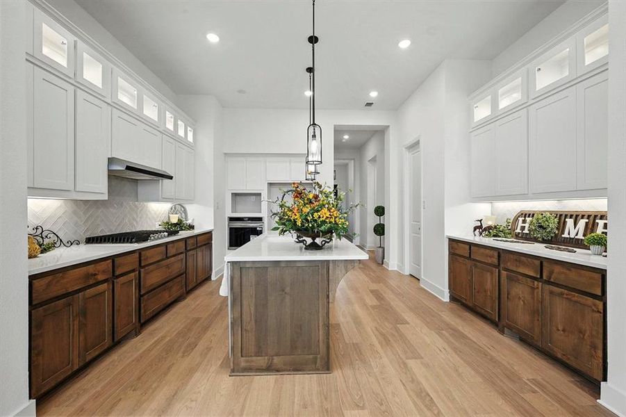 Kitchen featuring glass insert cabinets, hanging light fixtures, a center island with sink, decorative backsplash, and white cabinets
