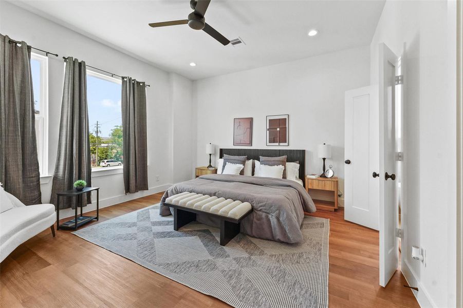 Spacious primary bedroom with large windows, wood flooring, modern ceiling fan, and ample natural light, creating a bright and relaxing retreat. Spacious primary bedroom with large windows, wood flooring, modern ceiling fan, and ample natural light, creating a bright and relaxing retreat.