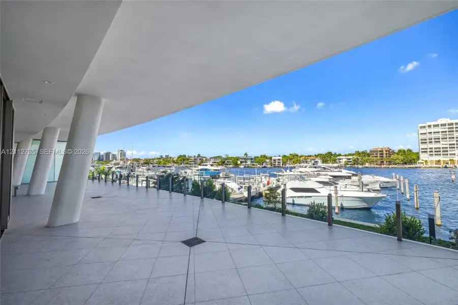 Covered terrace featuring large-format tile flooring, angled structural columns, and a direct water frontage with marina access