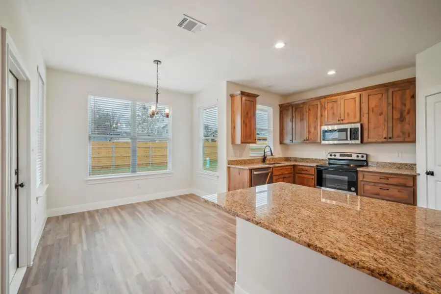 Kitchen with stainless steel appliances, brown cabinets, visible vents, and light wood finished floors