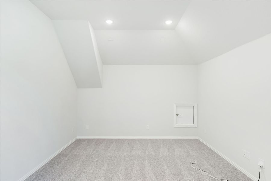 Empty room with angled ceiling, recessed lighting, gray carpet, and small access door on white wall