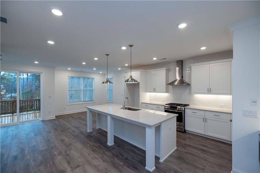 Kitchen featuring stainless steel gas range oven, pendant lighting, wall chimney range hood and stone countertops. Pictures represent a previously built home not the actual home, home is under construction.