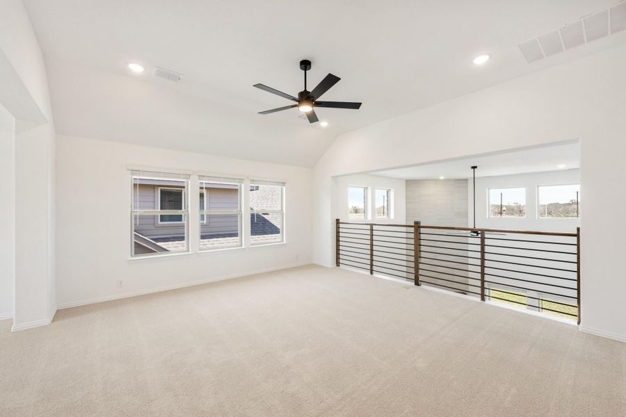 Open loft space with vaulted ceiling, ceiling fan, carpet flooring, and metal railing overlooking lower level