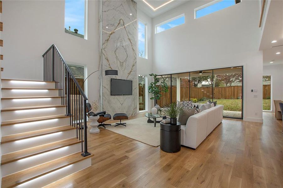Living room featuring a high ceiling, wood finished floors, plenty of natural light, and stairway Living room featuring a high ceiling, wood finished floors, plenty of natural light, and stairway