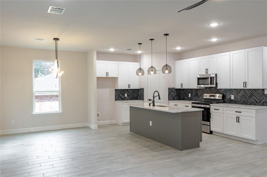 Kitchen with pendant lighting, sink, white cabinetry, and stainless steel appliances