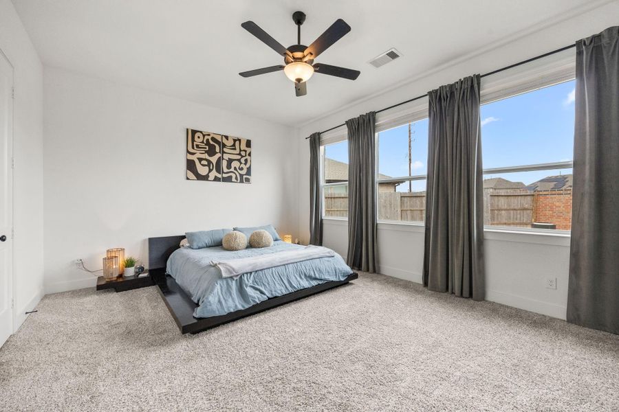 The primary suite features plush carpeting, high ceilings, and oversized windows with curtain rods already installed.