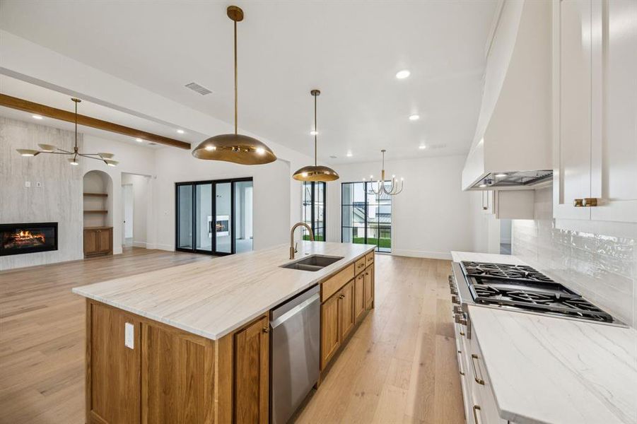 Kitchen with stainless steel dishwasher, brown cabinets, a fireplace, light wood-style flooring, and recessed lighting Kitchen with stainless steel dishwasher, brown cabinets, a fireplace, light wood-style flooring, and recessed lighting