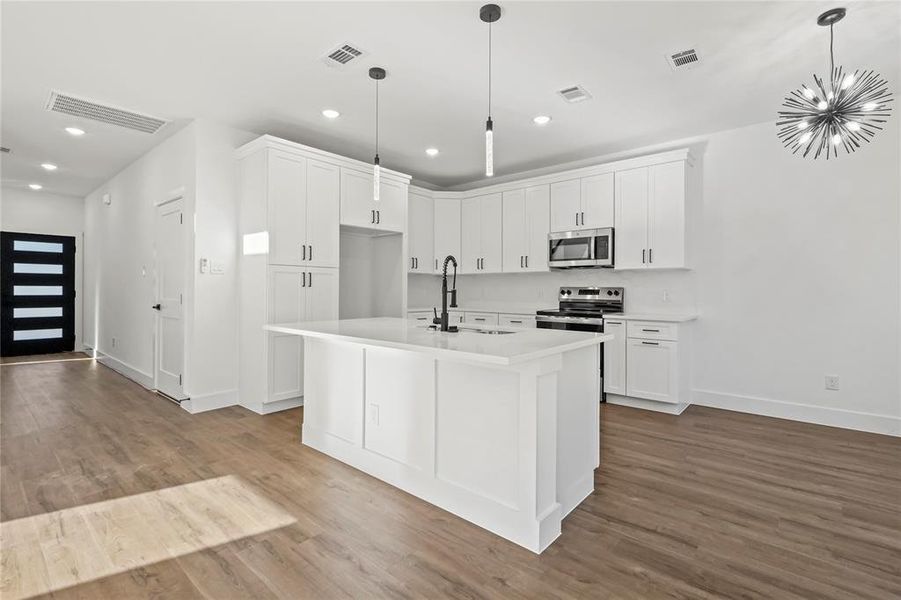 Kitchen with white cabinetry, decorative light fixtures, stainless steel appliances, a center island with sink, and dark wood finished floors