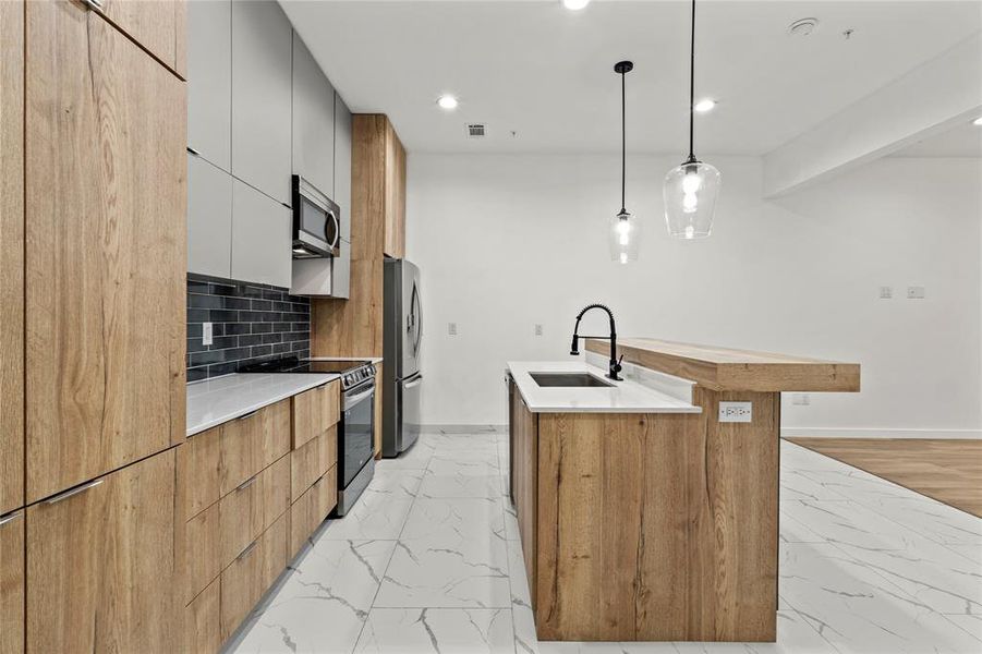 Kitchen with light marble finish flooring, modern cabinets, appliances with stainless steel finishes, a kitchen island with sink, and recessed lighting Kitchen with light marble finish flooring, modern cabinets, appliances with stainless steel finishes, a kitchen island with sink, and recessed lighting