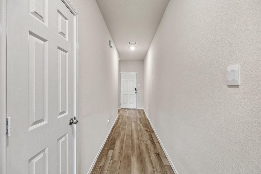 A well-lit hallway with durable wood flooring leads to the home's primary entrance.