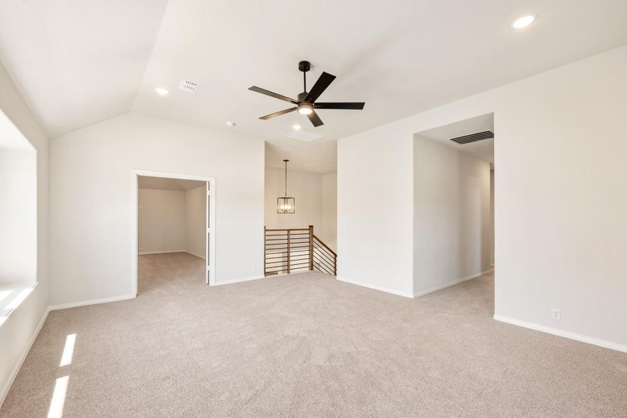 Open upstairs loft with vaulted ceiling, ceiling fan, carpet, and staircase railing visible Open upstairs loft with vaulted ceiling, ceiling fan, carpet, and staircase railing visible