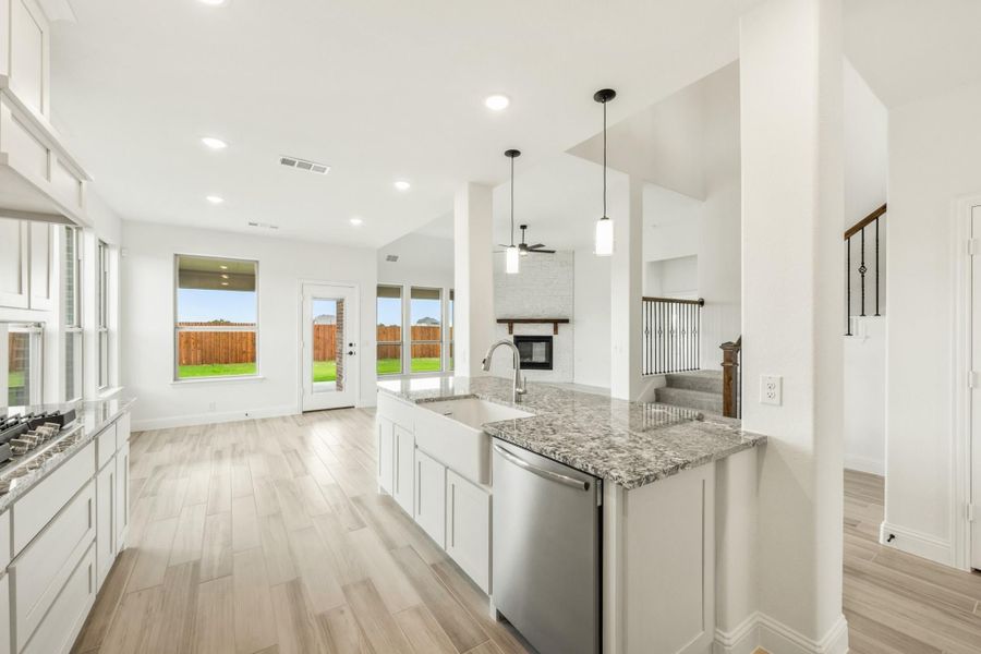 Open kitchen with white cabinets, granite island, farmhouse sink, and view into living room with fireplace Open kitchen with white cabinets, granite island, farmhouse sink, and view into living room with fireplace