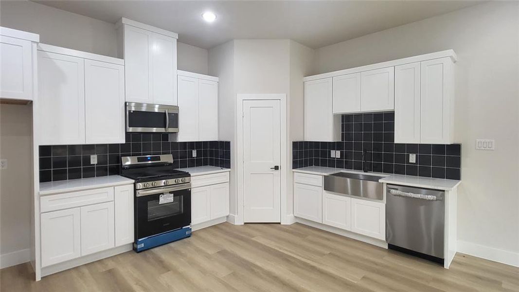 Kitchen featuring baseboards, appliances with stainless steel finishes, light wood finished floors, and light countertops