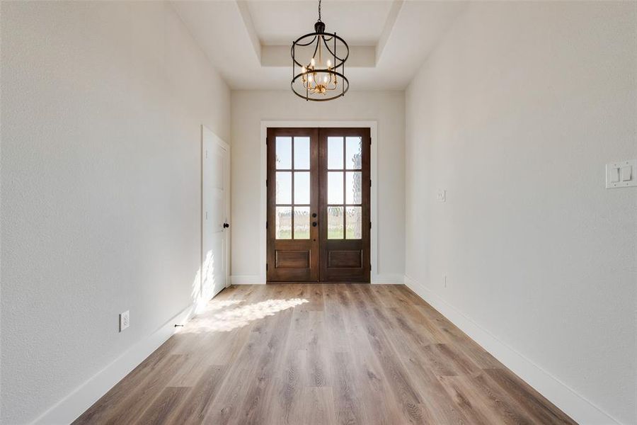 Entryway with a notable chandelier, light hardwood / wood-style floors, a tray ceiling, and french doors