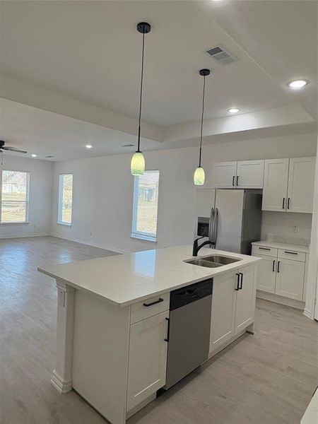 Kitchen with recessed lighting, white cabinets, fridge, pendant lighting, and an island with sink