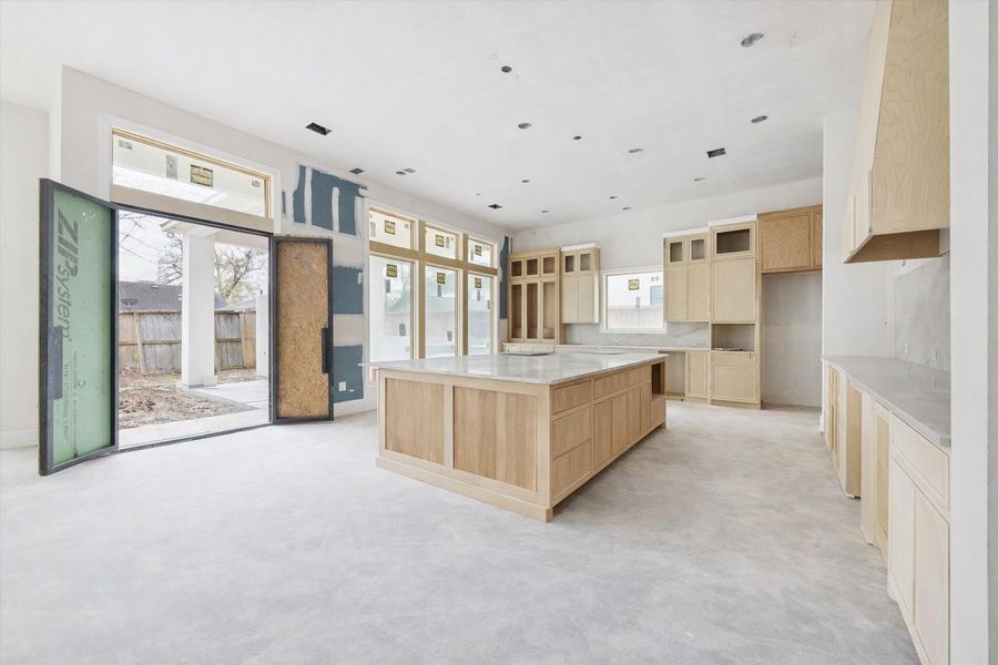 Chef-inspired kitchen featuring a large central island and an expansive bank of windows overlooking the private patio. This bright, modern space is designed with sleek contemporary cabinetry and premium finishes, offering a seamless flow for indoor-outdoor entertaining. Chef-inspired kitchen featuring a large central island and an expansive bank of windows overlooking the private patio. This bright, modern space is designed with sleek contemporary cabinetry and premium finishes, offering a seamless flow for indoor-outdoor entertaining.