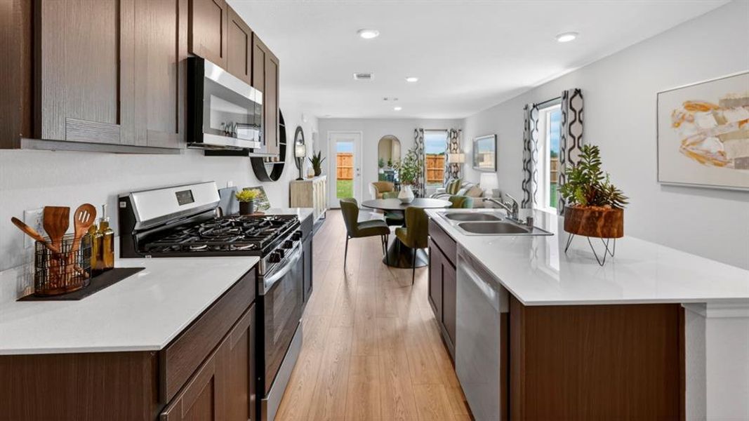 Modern kitchen featuring dark wood cabinetry, white countertops, stainless steel appliances, and wood-finish flooring Modern kitchen featuring dark wood cabinetry, white countertops, stainless steel appliances, and wood-finish flooring