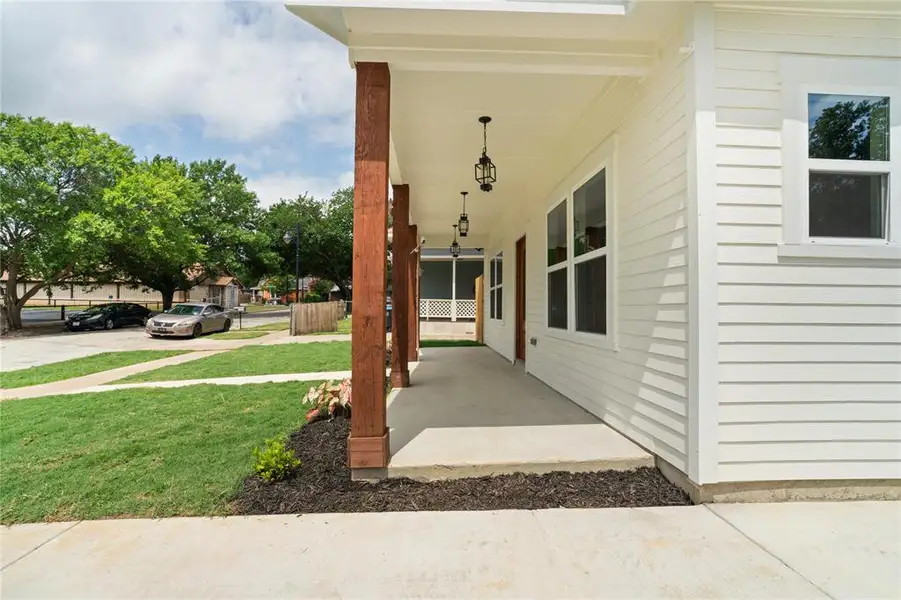 Inviting front porch featuring substantial wood-finish columns, pendant lighting, white horizontal siding, and multiple windows