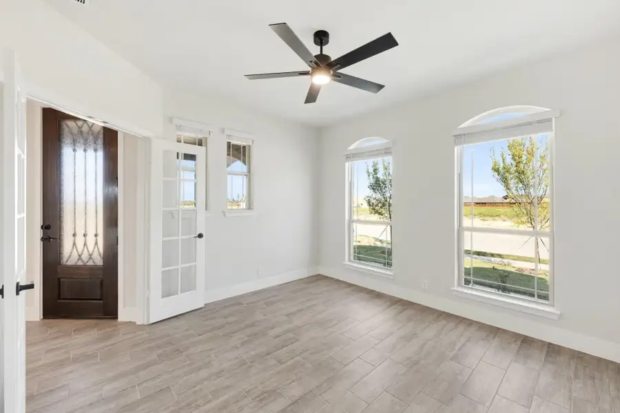 Empty room with wood-look tile floors, ceiling fan, arched windows, and dark wood front door with glass panel