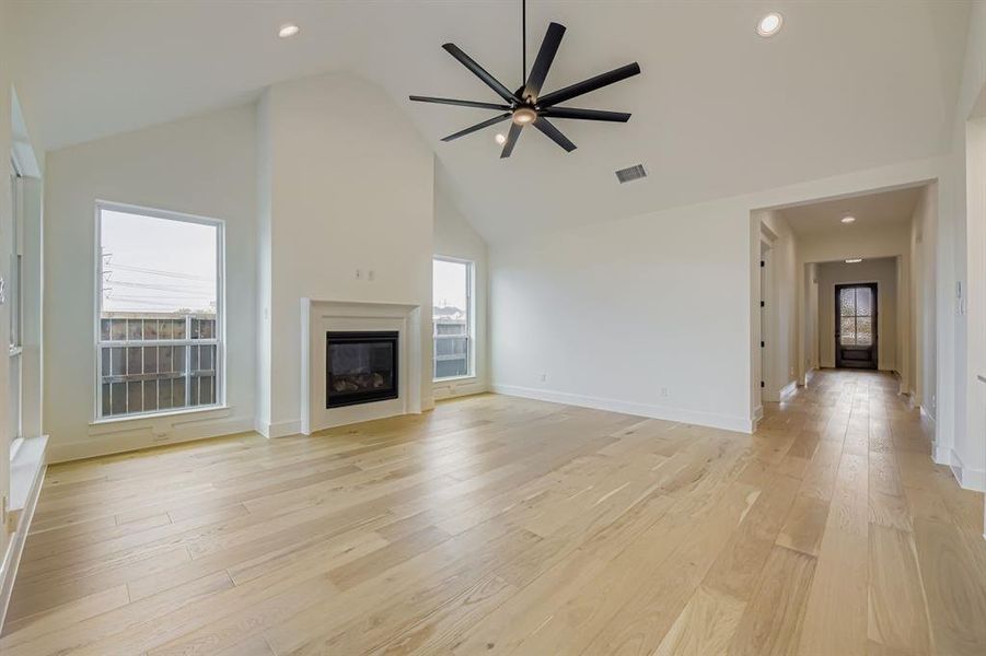 Unfurnished living room featuring light wood finished floors, high vaulted ceiling, a glass covered fireplace, recessed lighting, and a ceiling fan Unfurnished living room featuring light wood finished floors, high vaulted ceiling, a glass covered fireplace, recessed lighting, and a ceiling fan