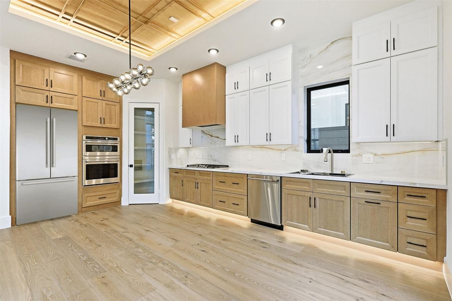 High-end finishes include a built-in stainless steel refrigerator, double ovens, and stone countertops with a matching full-height backsplash.