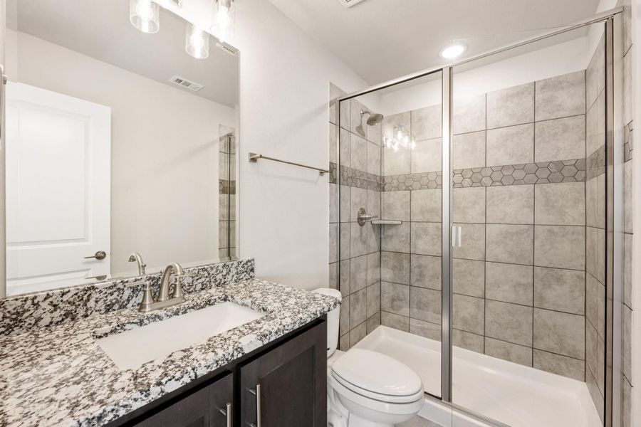 Bathroom with granite countertop vanity, glass-enclosed tiled shower, and white toilet