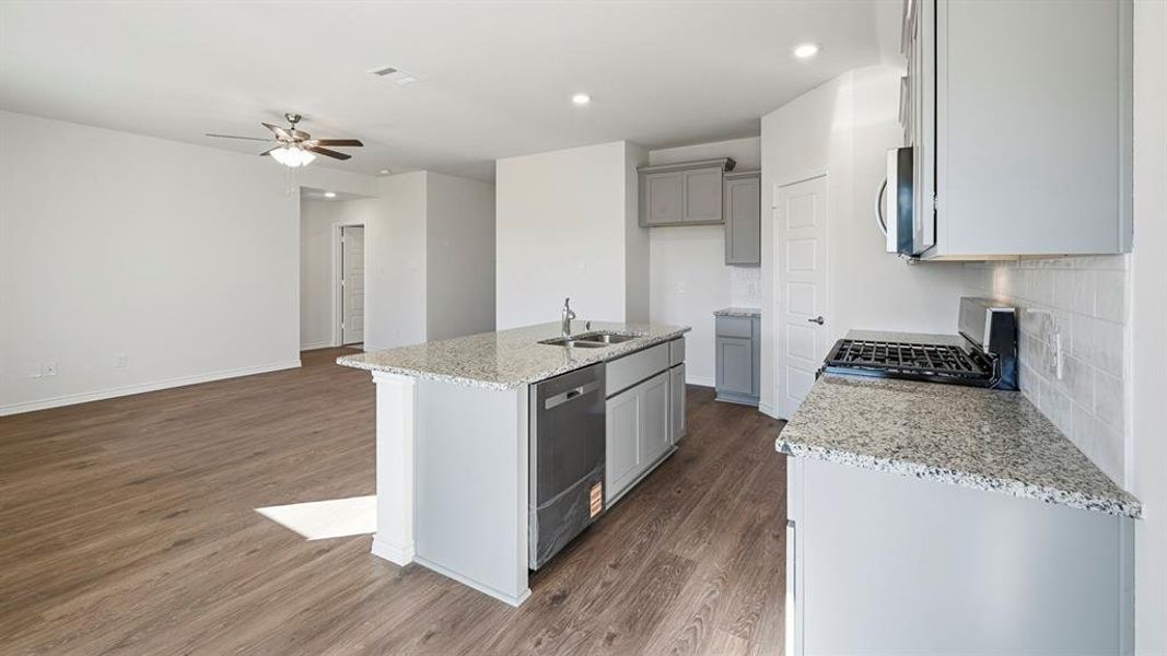 The kitchen features an island with a stainless steel sink and dishwasher, granite countertops, and grey cabinetry