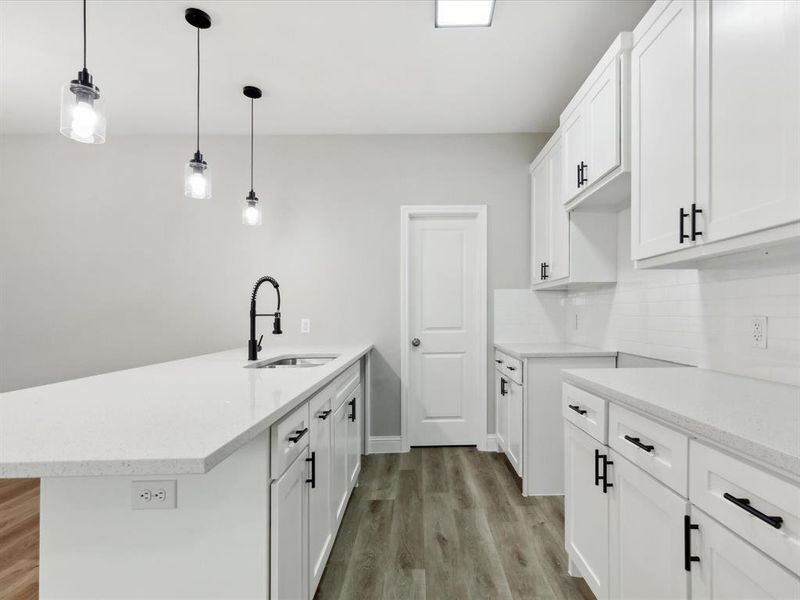 Kitchen featuring white cabinetry, light wood-type flooring, decorative light fixtures, backsplash, and sink