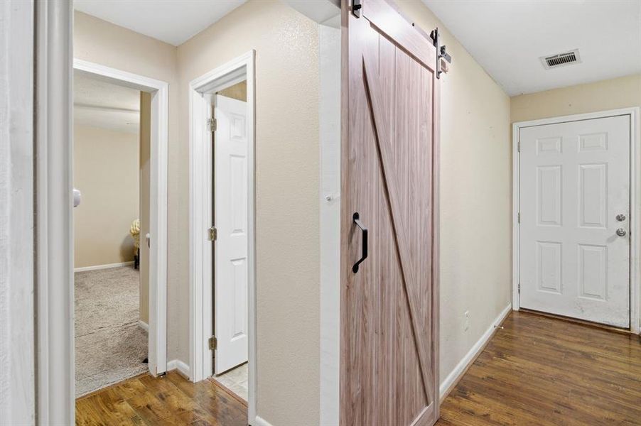Hallway featuring wood-finish flooring, light-toned walls, and a contemporary barn door with black hardware