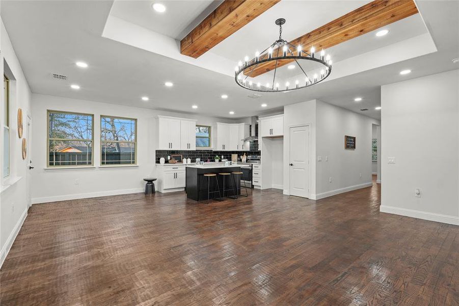Unfurnished living room with beamed ceiling, hanging lights, and dark wood-style floors