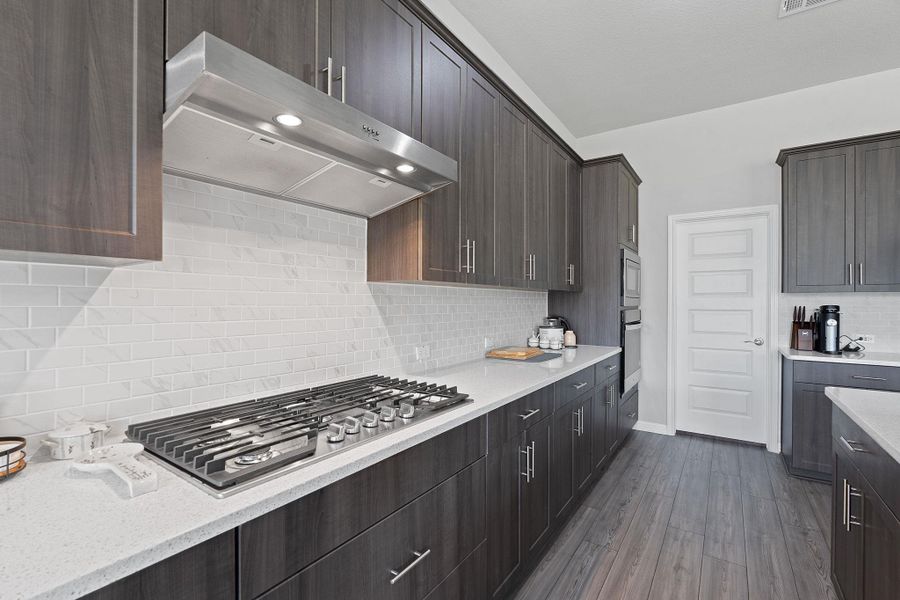 Kitchen featuring light stone counters, tasteful backsplash, dark brown cabinets, stainless steel appliances, and ventilation hood Kitchen featuring light stone counters, tasteful backsplash, dark brown cabinets, stainless steel appliances, and ventilation hood