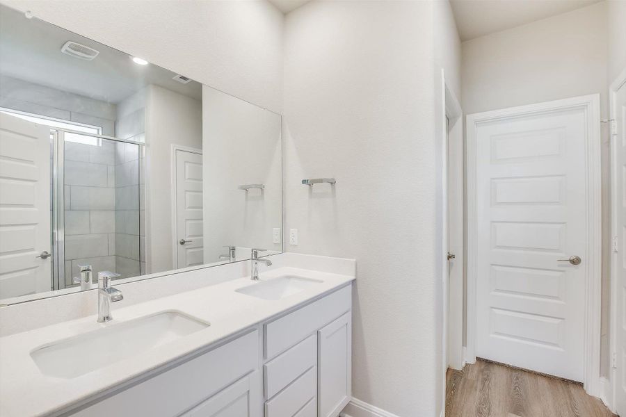 Bathroom featuring double vanity, a sink, a shower stall, and wood finished floors