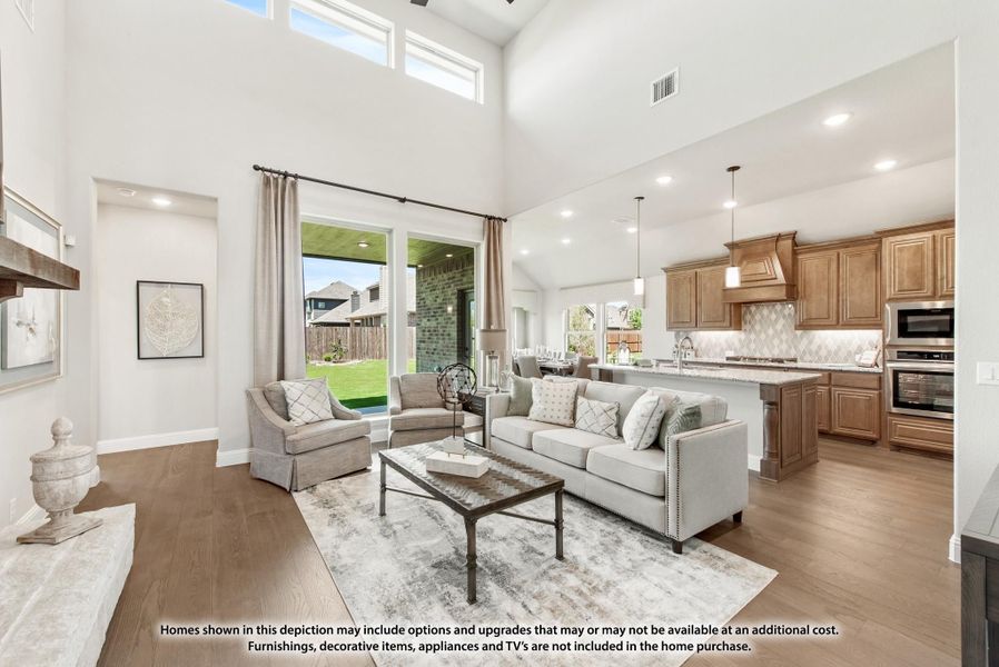 Open-concept living room with two-story ceiling, hardwood floors, and kitchen visible in background Open-concept living room with two-story ceiling, hardwood floors, and kitchen visible in background
