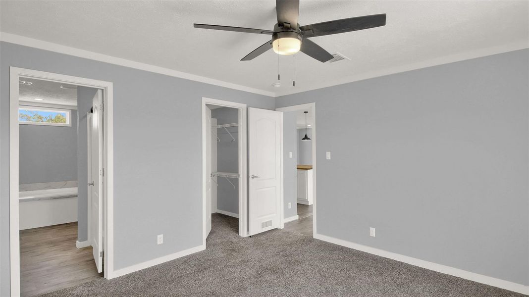 Plush carpeting and crown molding define this serene bedroom space with adjacent closets.