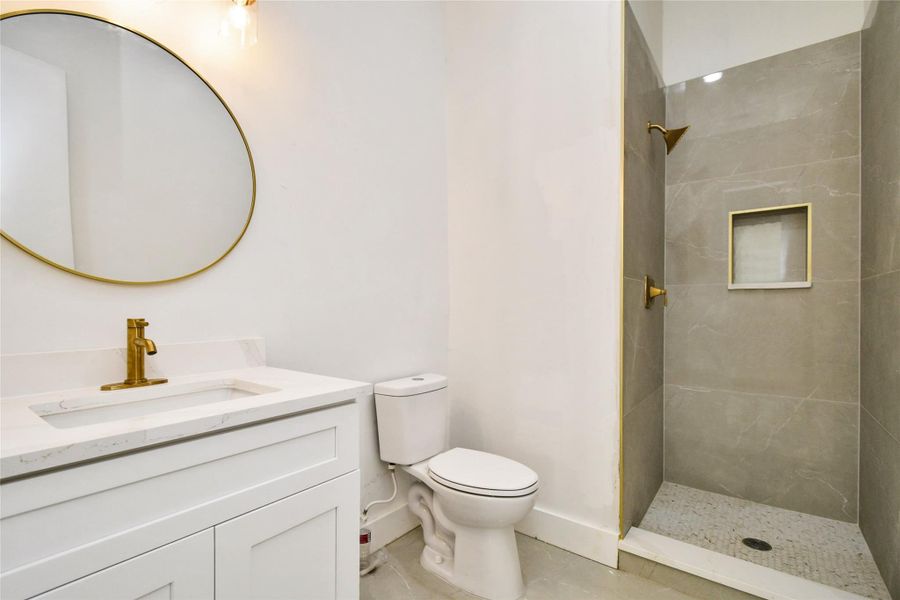 A sleek contemporary bathroom featuring a quartz-topped vanity with a gold-tone faucet, a designer circular mirror, and a walk-in shower with sophisticated large-format tile and a mosaic floor.