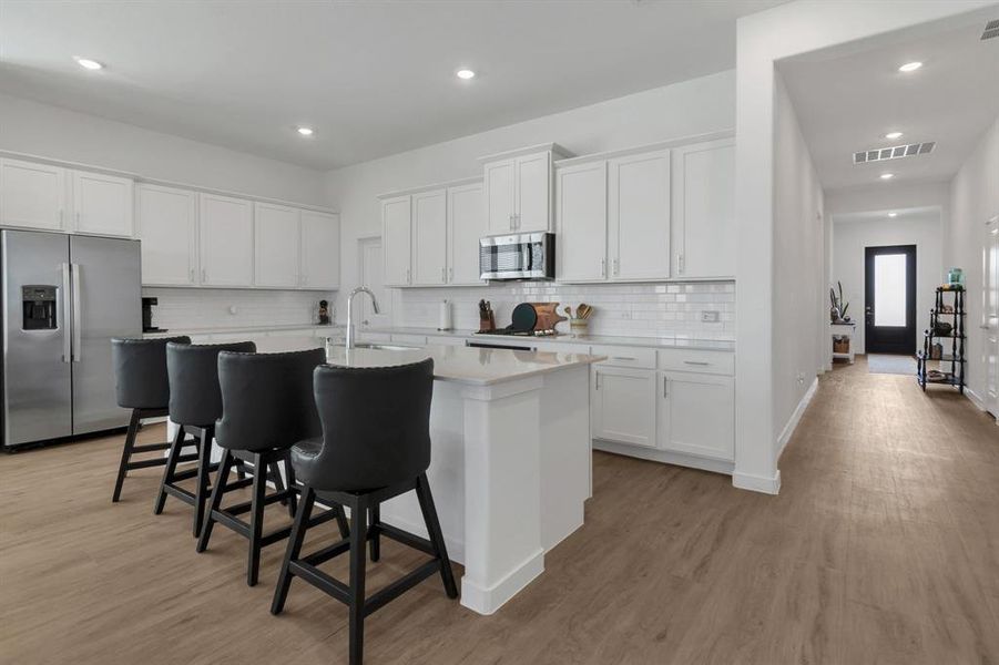 Kitchen featuring white cabinetry, stainless steel appliances, an island with sink, light wood-style flooring, and recessed lighting
