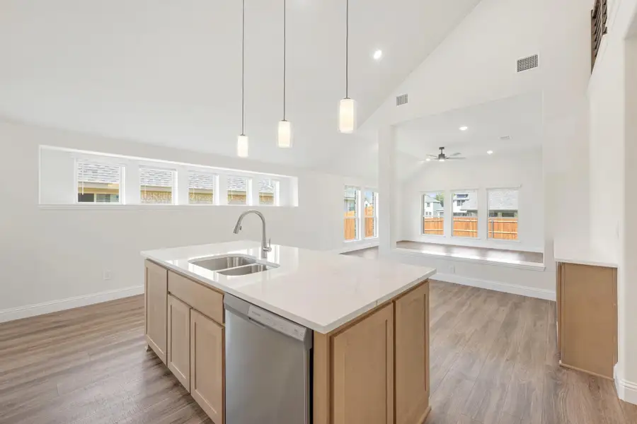 Kitchen island with sink, pendant lights, and vaulted ceiling open to living area with hardwood floors