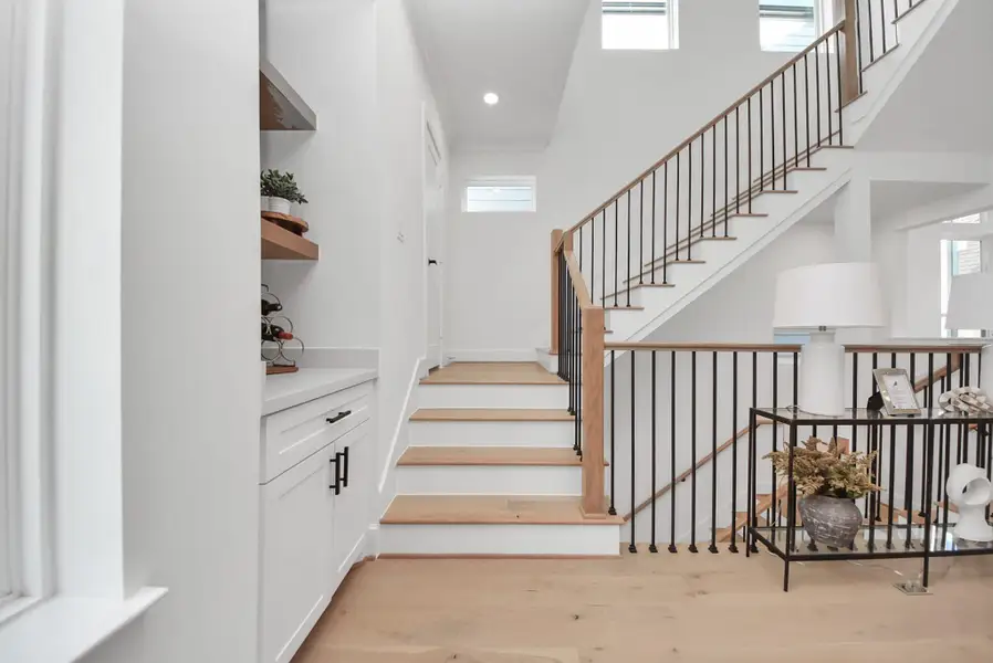 Ascend this bright, modern staircase with wooden steps and sleek metal railings. A built-in cabinet with open shelving and decorative touches like plants and a lamp create a welcoming and stylish entryway. Ascend this bright, modern staircase with wooden steps and sleek metal railings. A built-in cabinet with open shelving and decorative touches like plants and a lamp create a welcoming and stylish entryway.