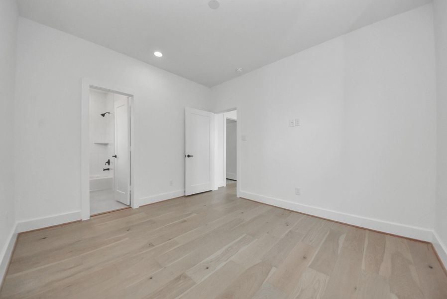 A clean, bright room with light wood flooring, white walls, and recessed lighting features two doors, one leading to a bathroom. The space’s modern, neutral design provides a versatile layout ready for personal touches. A clean, bright room with light wood flooring, white walls, and recessed lighting features two doors, one leading to a bathroom. The space’s modern, neutral design provides a versatile layout ready for personal touches.