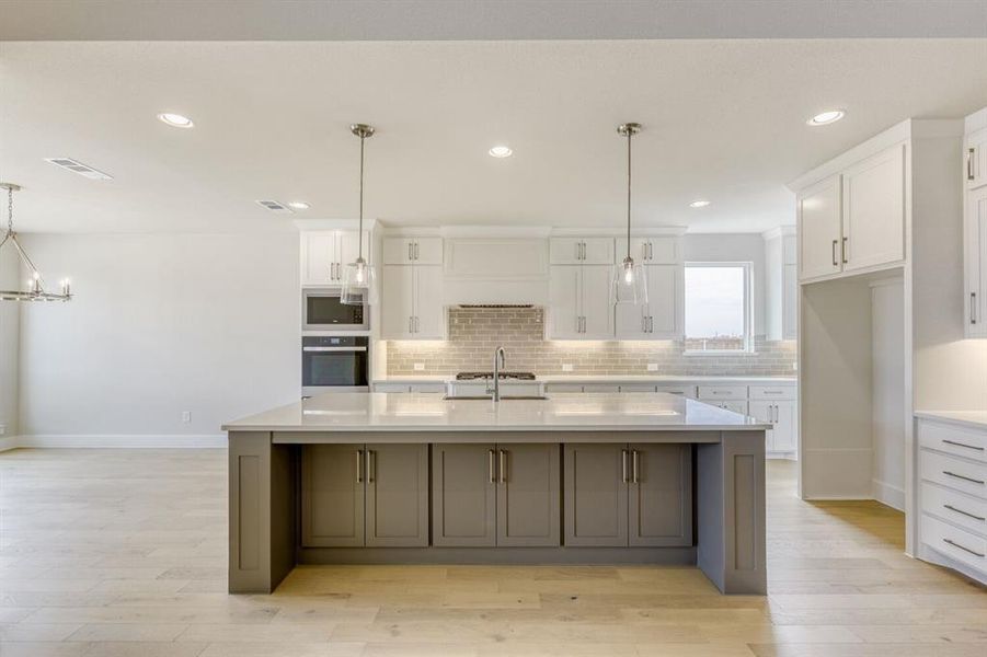 Kitchen with pendant lighting, a large island with sink, light wood-type flooring, stainless steel appliances, and light stone countertops