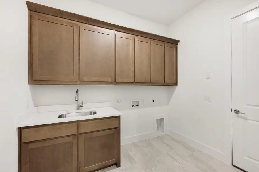 Laundry room with wood upper cabinets, utility sink, and washer and dryer hookups on light tile floor Laundry room with wood upper cabinets, utility sink, and washer and dryer hookups on light tile floor