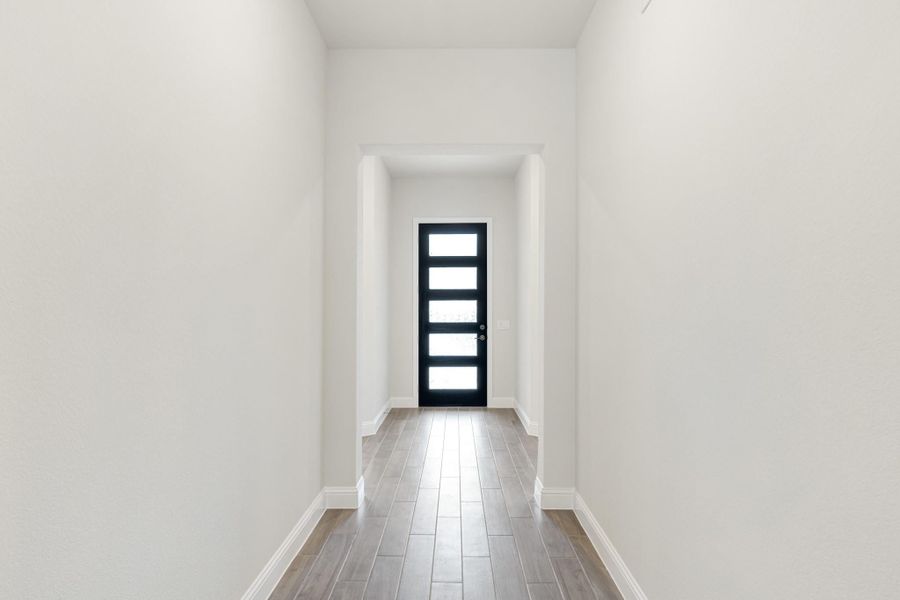Narrow entryway hallway with wood-look tile floors, white walls, and a black front door with glass panels Narrow entryway hallway with wood-look tile floors, white walls, and a black front door with glass panels