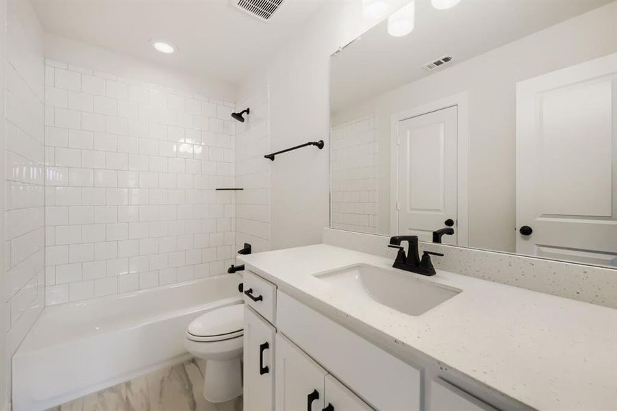 Bathroom featuring a white subway tile shower surround, a built-in tub, white vanity cabinetry with black hardware, a light-toned countertop with an integrated sink, and black fixtures Bathroom featuring a white subway tile shower surround, a built-in tub, white vanity cabinetry with black hardware, a light-toned countertop with an integrated sink, and black fixtures