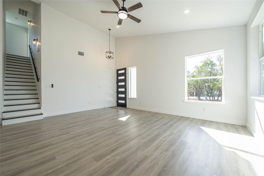 Unfurnished living room featuring healthy amount of natural light, stairs, light wood-type flooring, ceiling fan, and a high ceiling