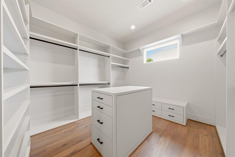 Boutique-style primary closet with custom built-ins, center island storage, and natural light.