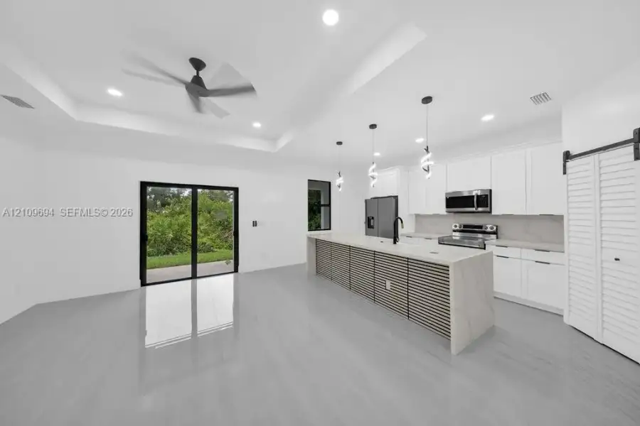 Kitchen featuring white cabinetry, an expansive island with slatted detail and stone-finish countertop, recessed lighting, polished large-format tile flooring, and a tray ceiling