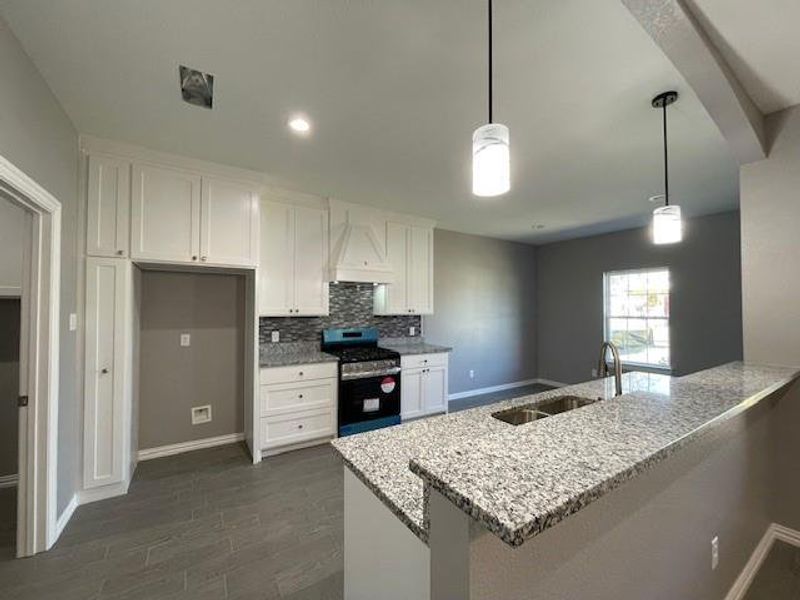 Kitchen with granite countertop, backsplash, stainless steel range with gas cooktop, white cabinets, and a sink Kitchen with granite countertop, backsplash, stainless steel range with gas cooktop, white cabinets, and a sink